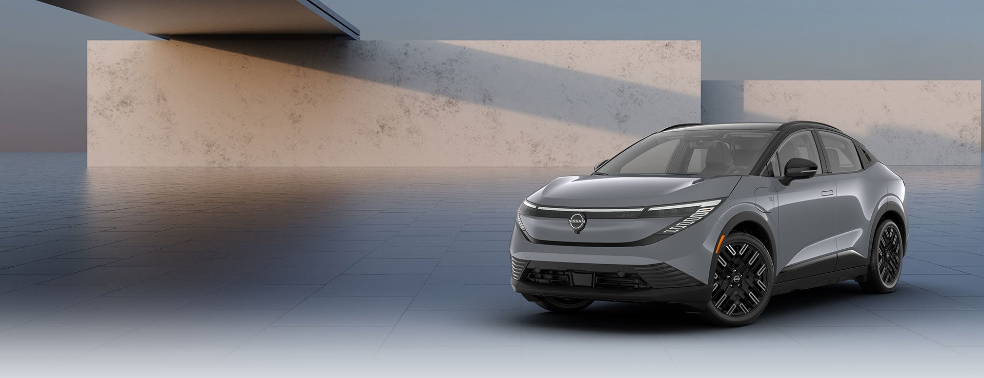 A gray Nissan Ariya EV is shown head-on. The sleek car has a black roof, side mirrors, and wheels.